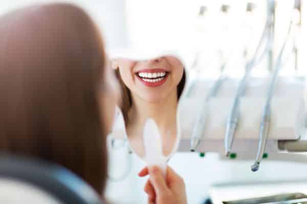 Paciente observando o próprio sorriso no espelho após o tratamento, representando o resultado estético alcançado com o Implante Zigomático.